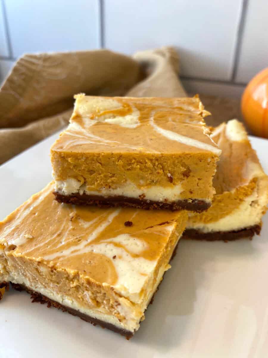 Three pumpkin cheesecake bars stacked on a plate.