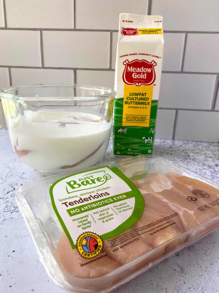 A package of chicken tenders with a glass bowl in the background filled with buttermilk