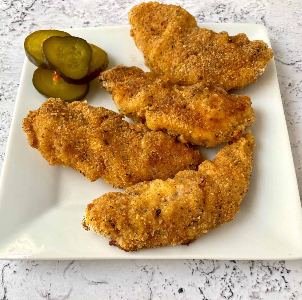 Chicken strips on a serving plate with pickles on the side