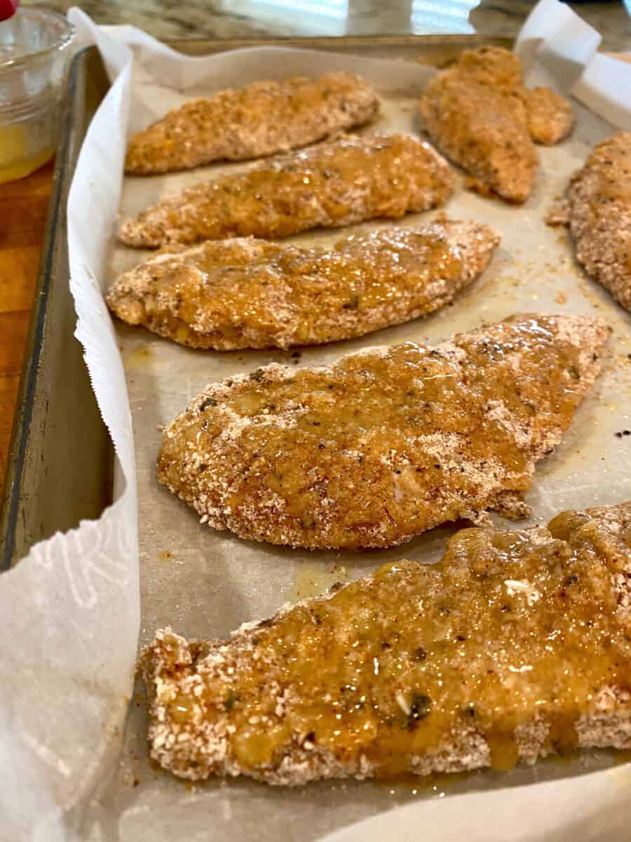 Chicken on parchment paper with a coating on melted butter covering the breaded strips