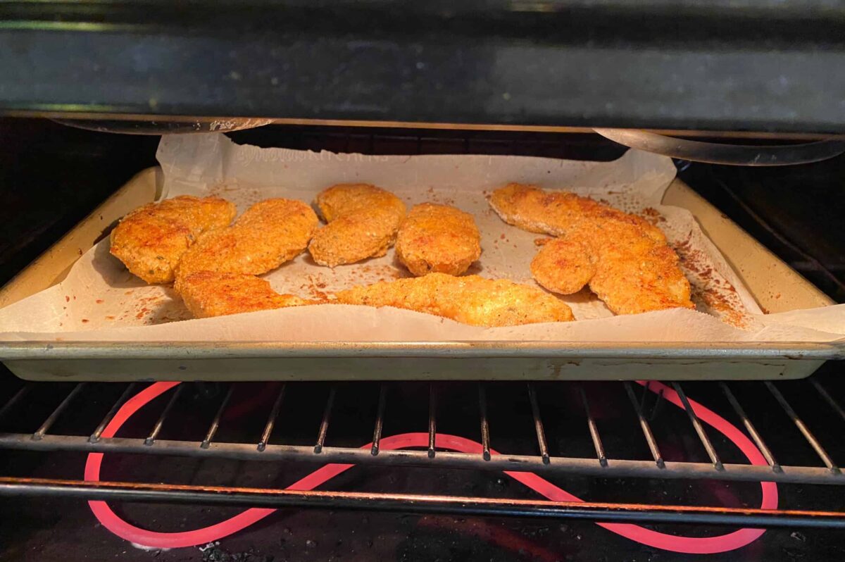 Buttermilk chicken strips on parchment paper, on a baking sheet, in the oven.