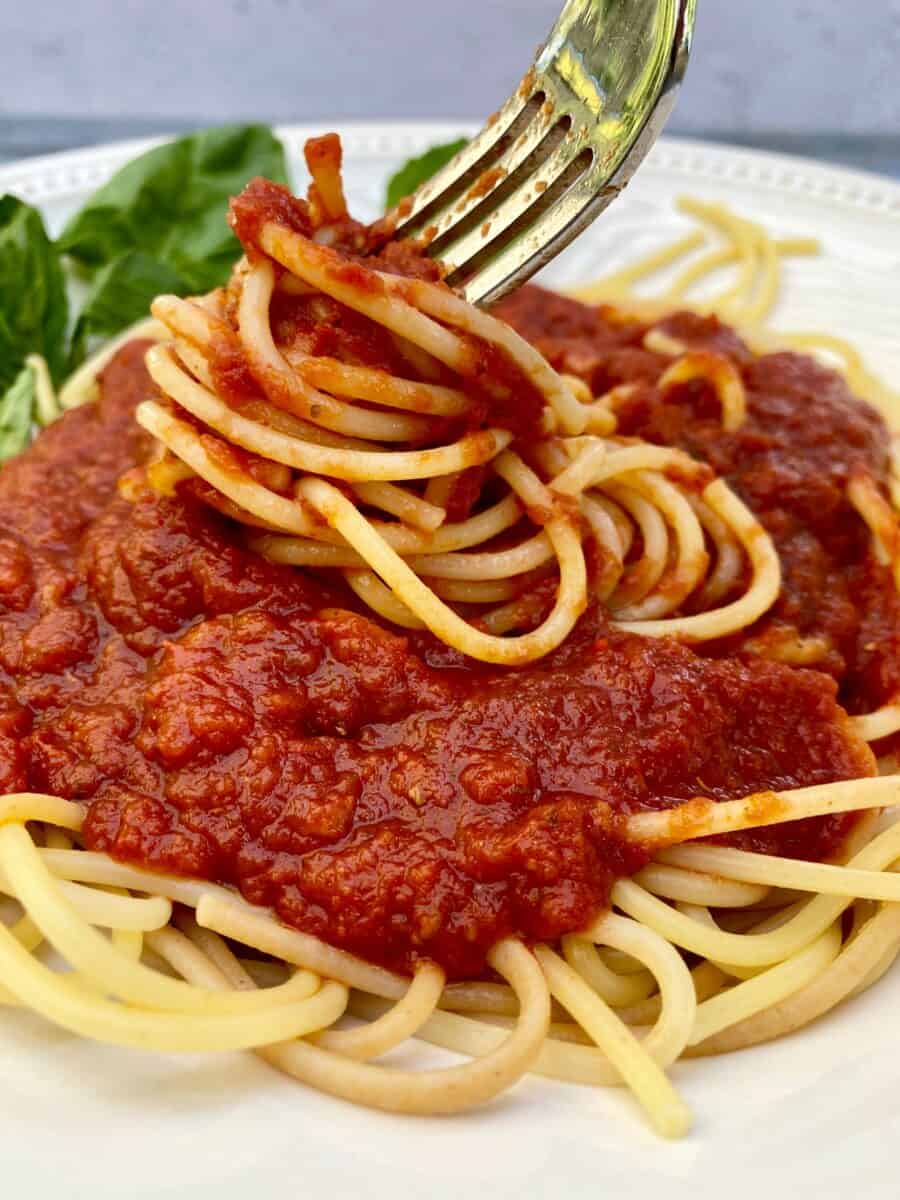 A plate with spaghetti and sauce on top with a fork scooping up some pasta to create a serving