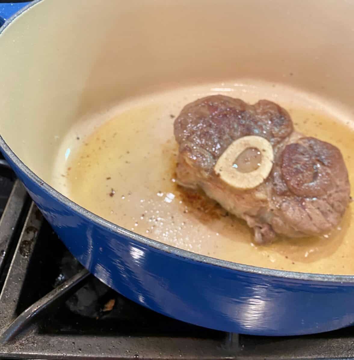 Beef shank browning in a pot with olive oil on a stove