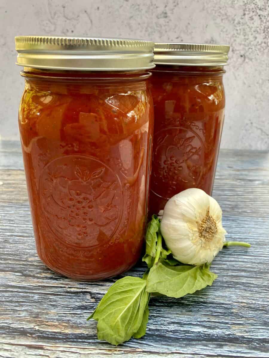 Two jars of spaghetti sauce next to a clove of garlic and fresh basil leaves