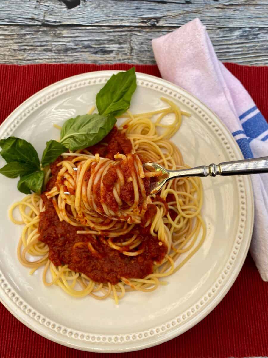 Spaghetti sauce and pasta noodles on a plate with a fork, basil on the edge and a napkin