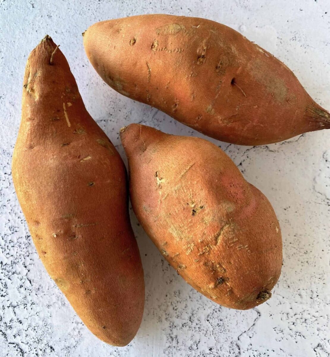 Three unpeeled sweet potatoes on a counter