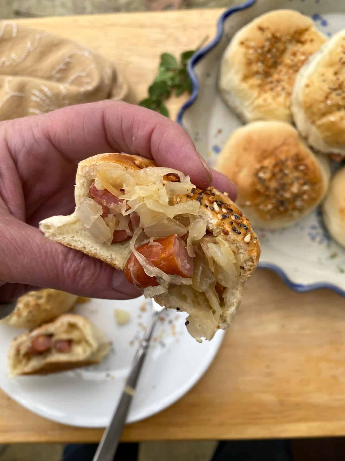 A hand holding a dinner roll with sausage and kraut filling