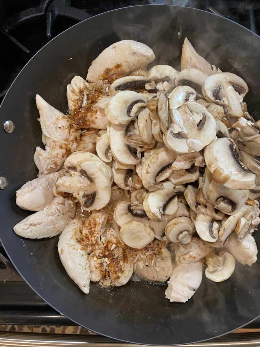 Mushrooms on top of cooked chicken and seasoning in a skillet