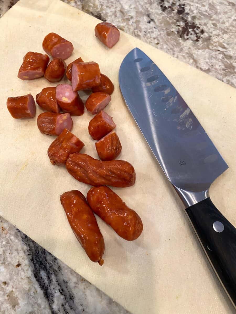 Diced little smokies on a small cutting board with a knife on the side