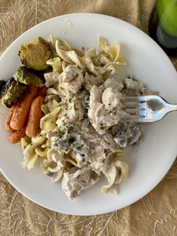A serving of chicken stroganoff on a plate with carrots and brussels sprouts on the side