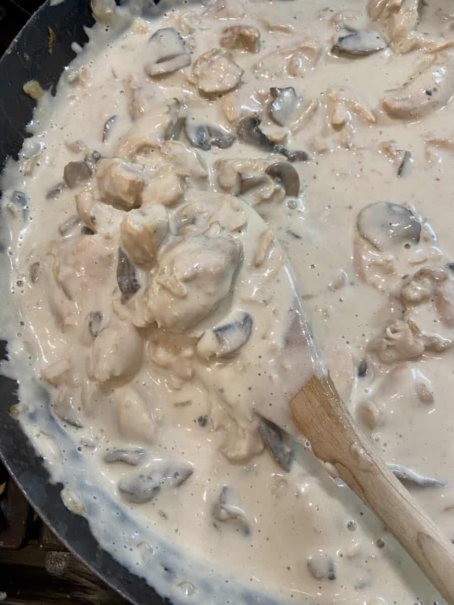 Stroganoff cooking in a skillet on the stove with a wooden spoon stirring the contents