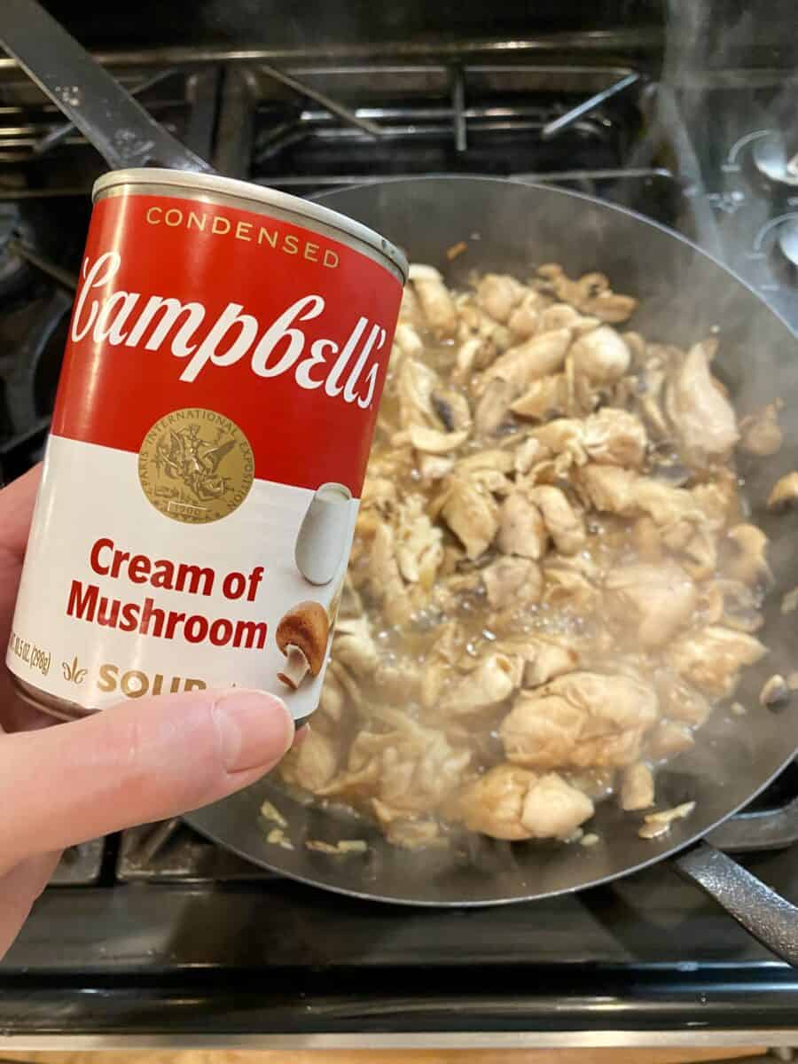 A can of cream of mushroom held over a pan of sauce.