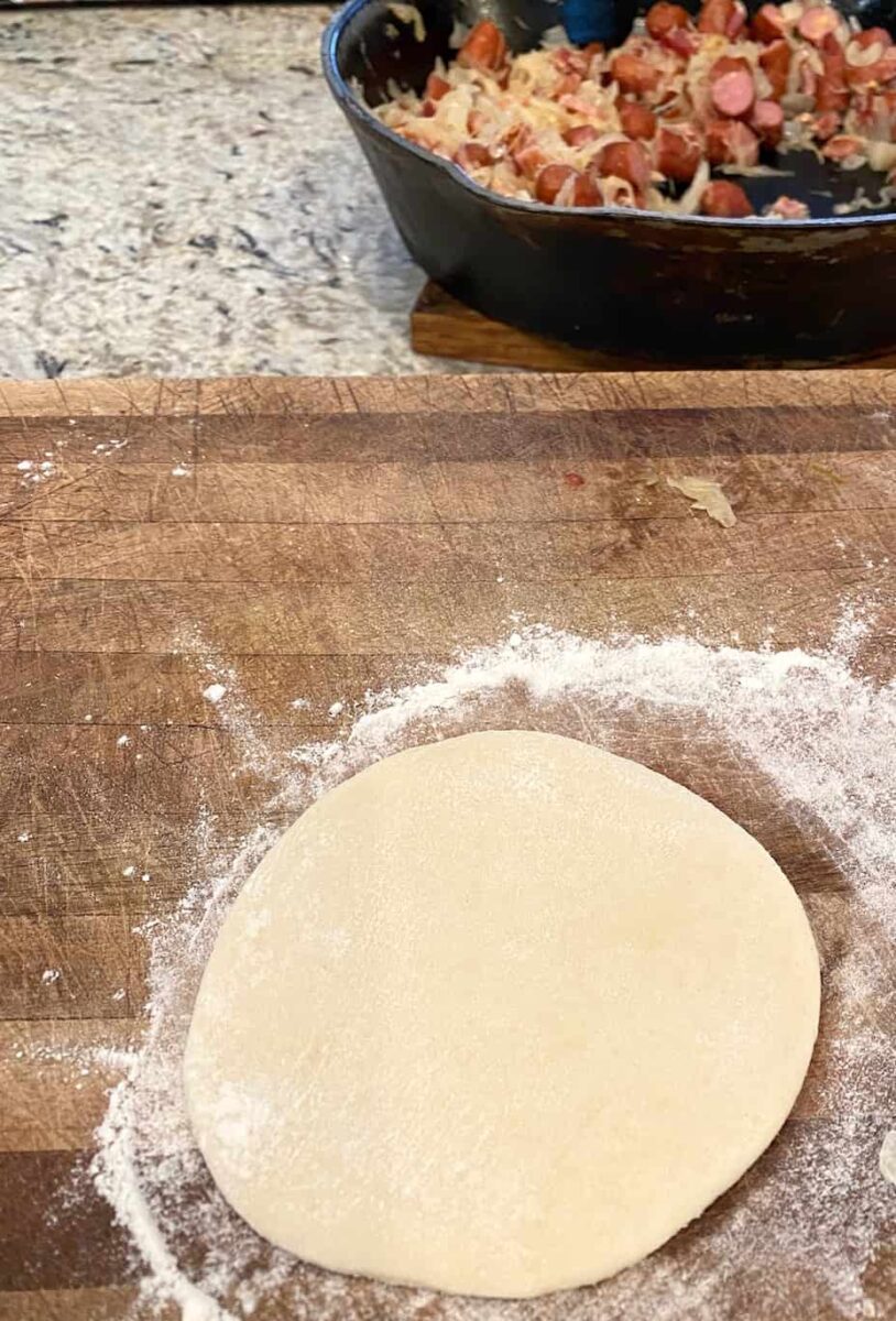 Dough rolled into a circle with a skillet on the side