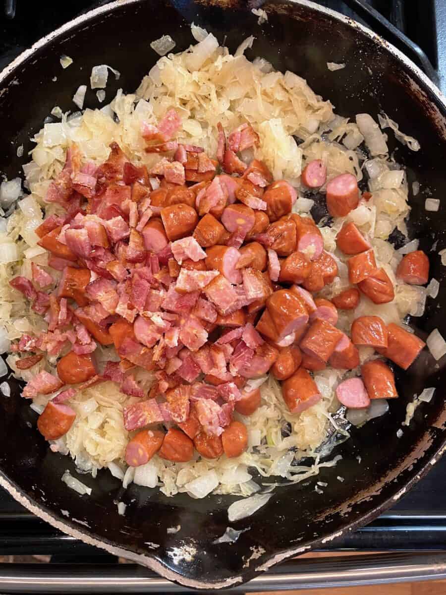 Onions, sauerkraut with little smokies on top, in a cast iron skillet on the stove