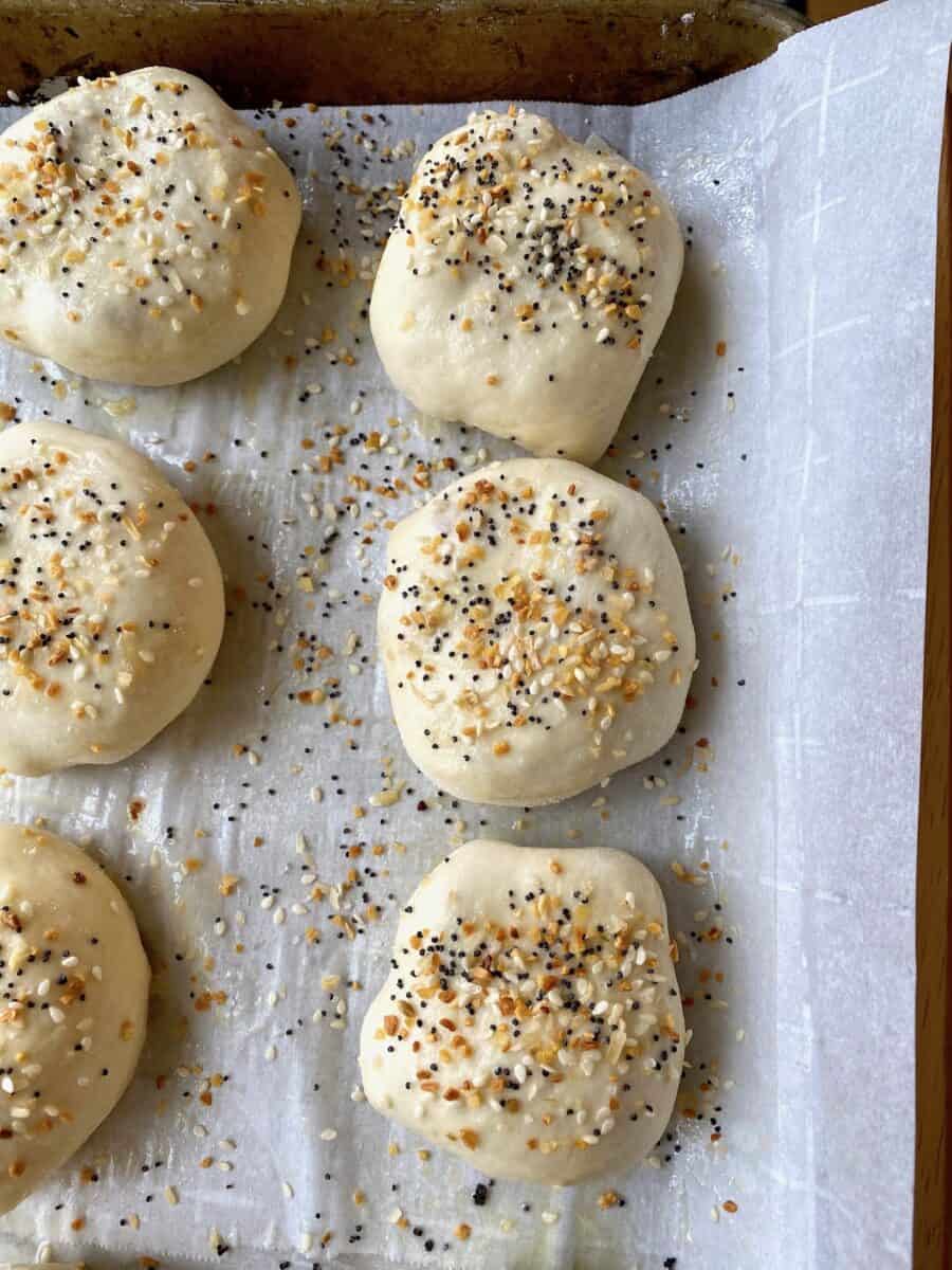 Stuffed dinner rolls with a sprinkling of everything bagel seasoning  top, placed on a baking sheet 