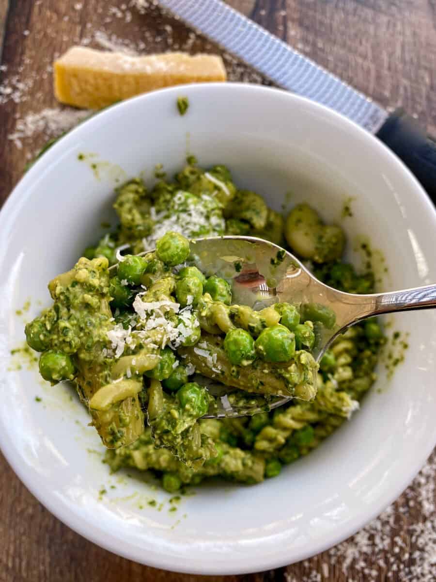 Pesto pasta salad being served from a bowl with parmesan cheese on top