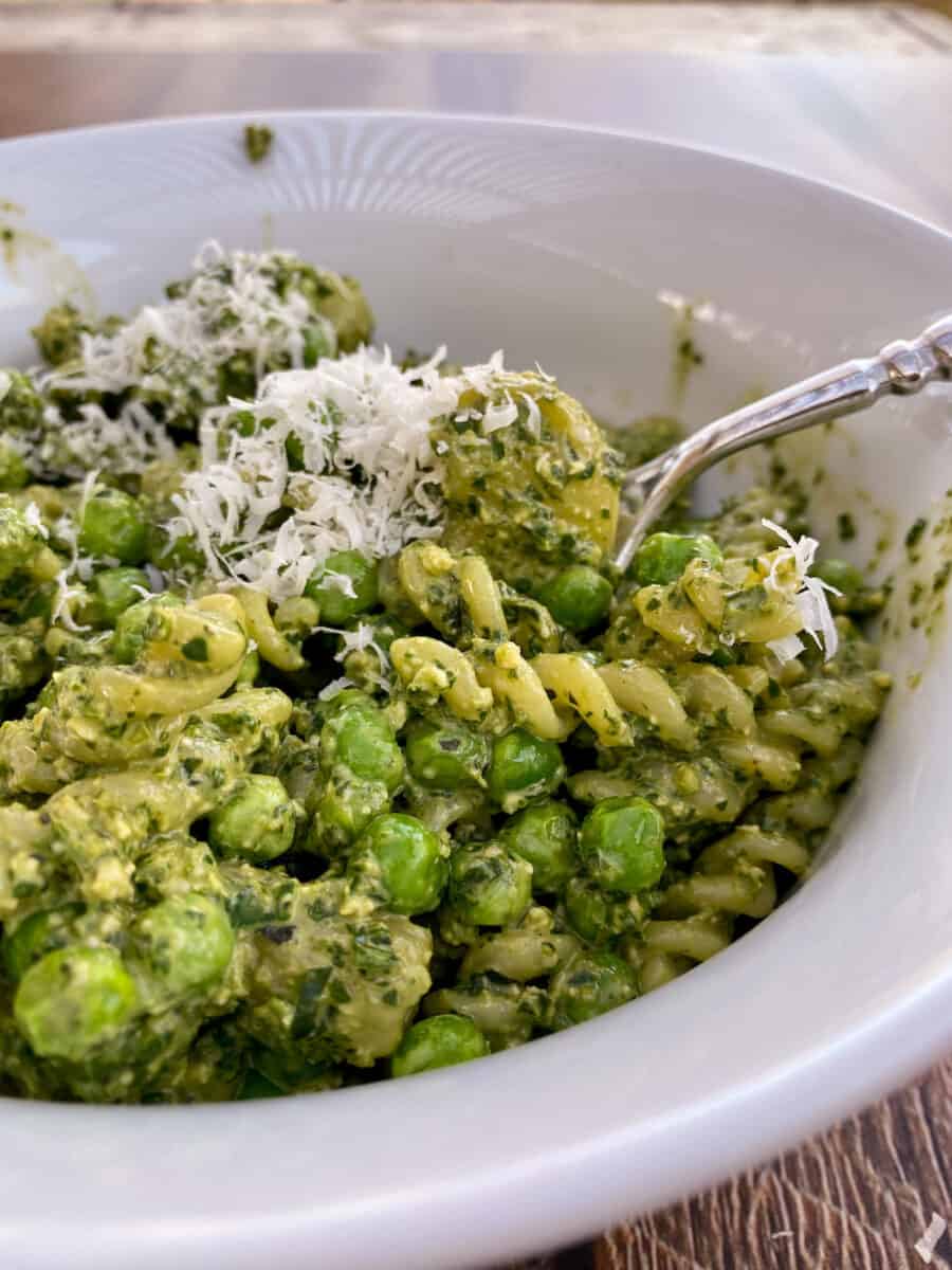 A bowl of pesto pasta salad with a serving spoon on the side