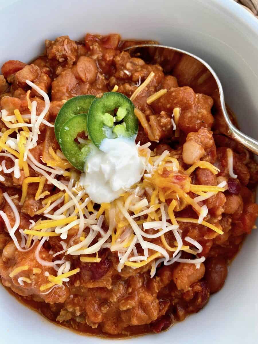 A bowl of chili with toppings and a spoon on the side