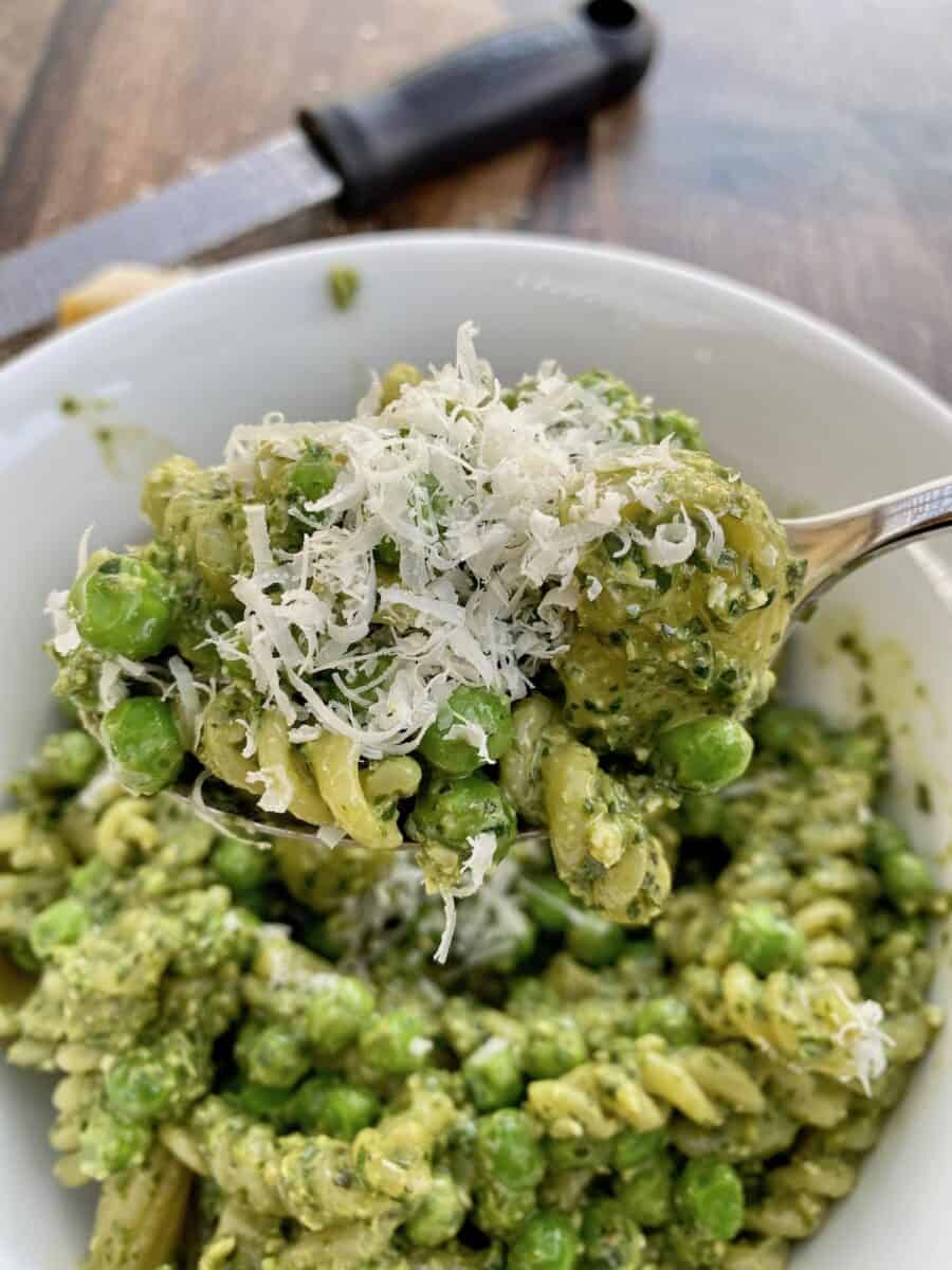 A bowl of pesto pasta salad with parmesan cheese shredded on top 