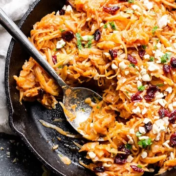 Braised cabbage and apples in a skillet with a spoon