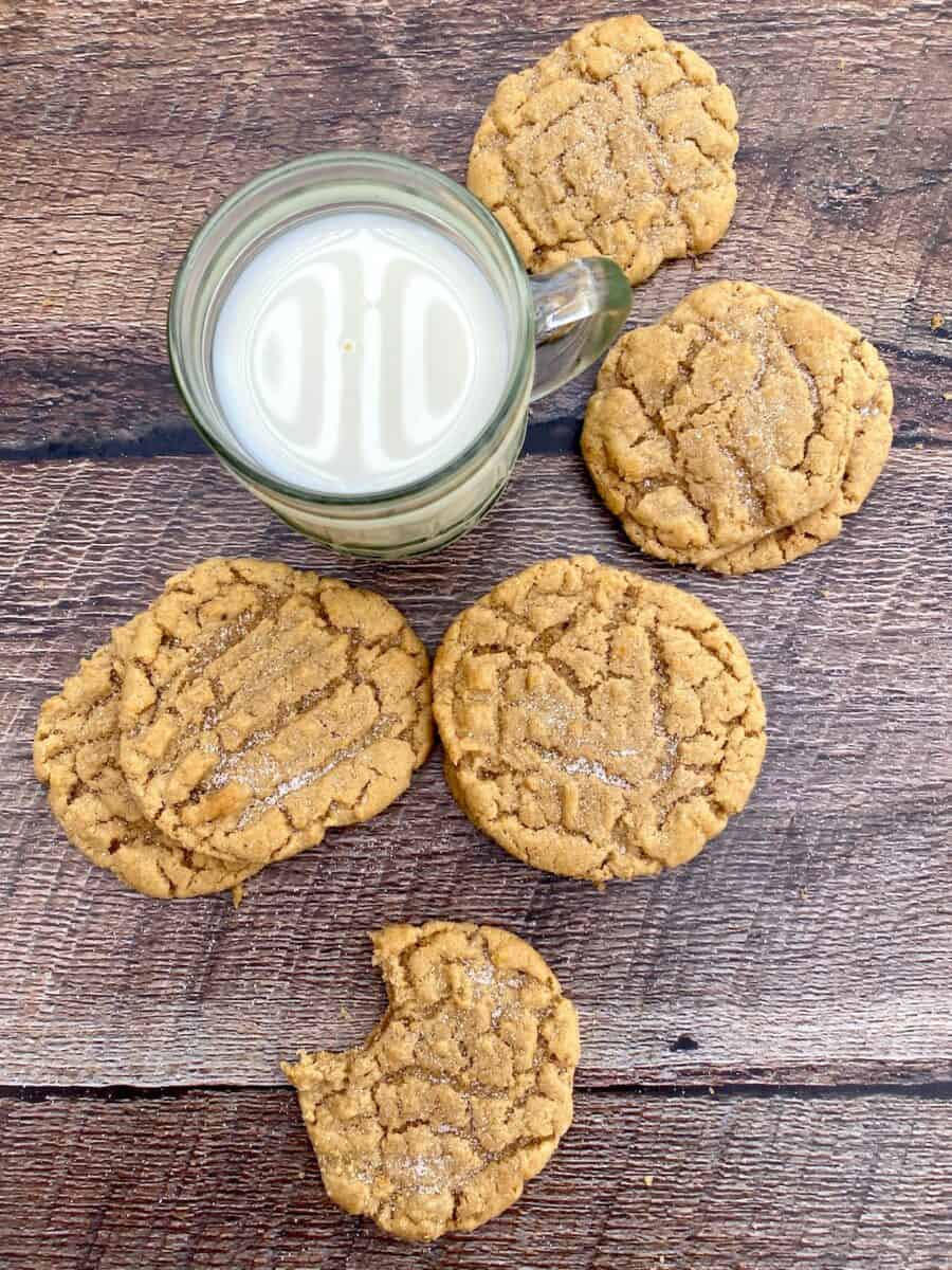 Six peanut butter cookies arranged on a wooden board next to a glass of milk.