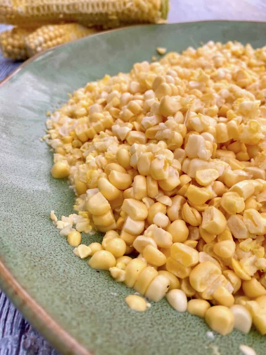 Fresh corn on a large plate with corn cobs in the distance.