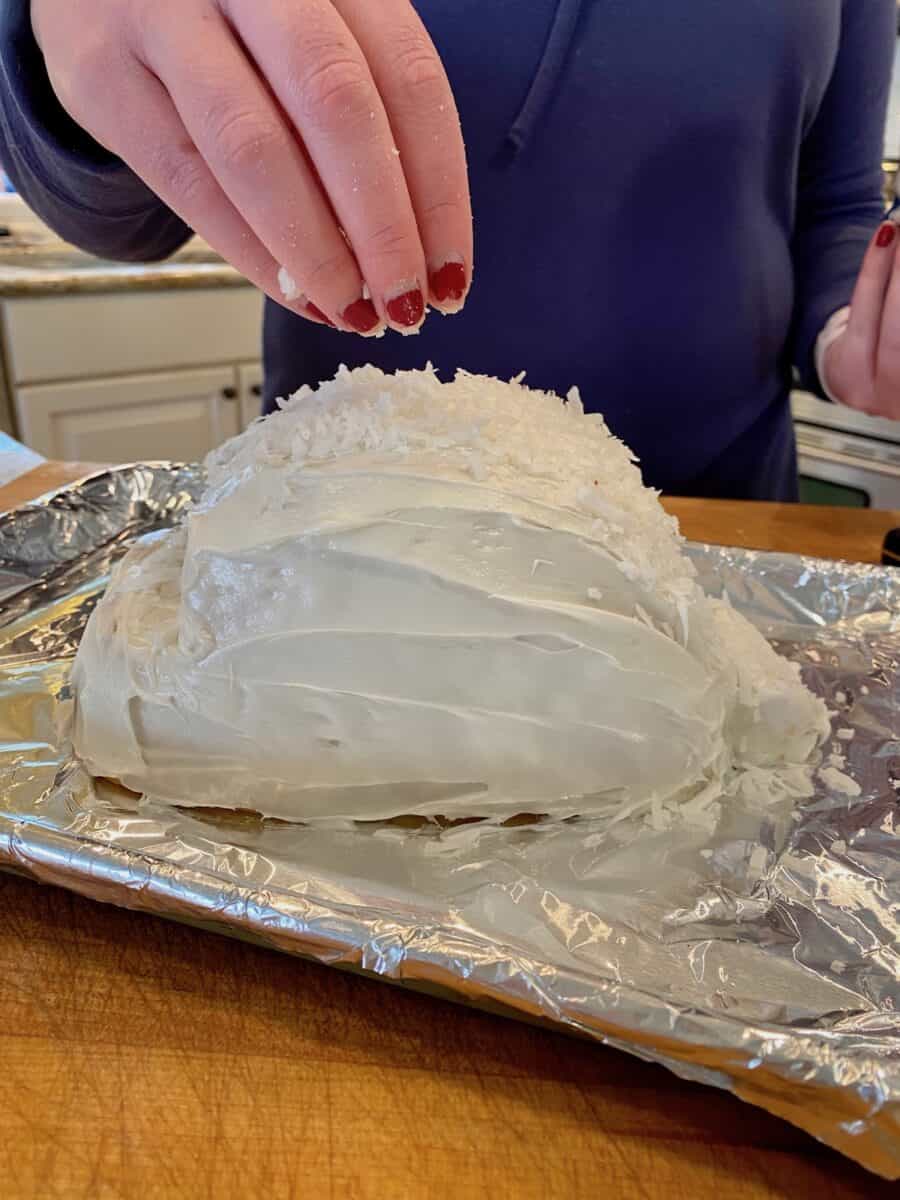 Adding shredded coconut to a frosted cake. 