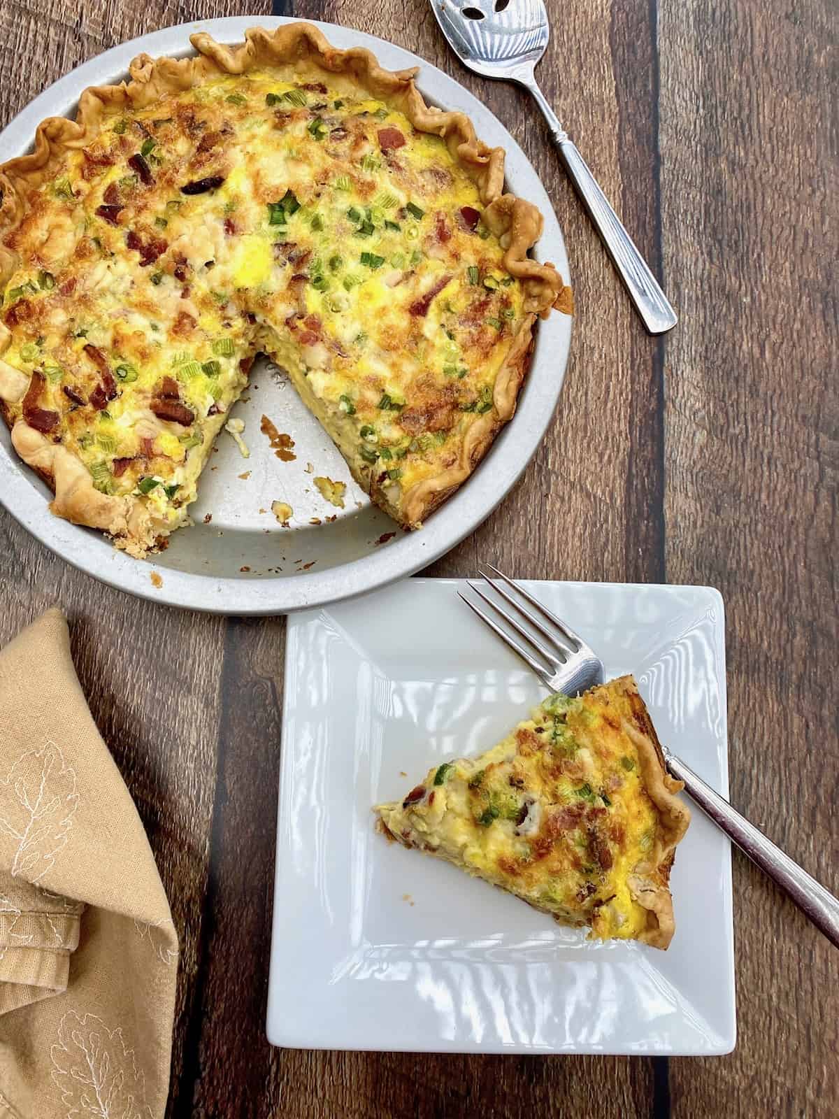 A wedge of cougar gold cheese on a small plate next to dish of quiche. 