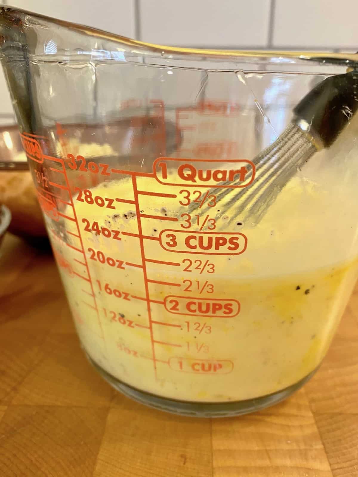 Eggs and milk whisked together in a glass measuring cup.