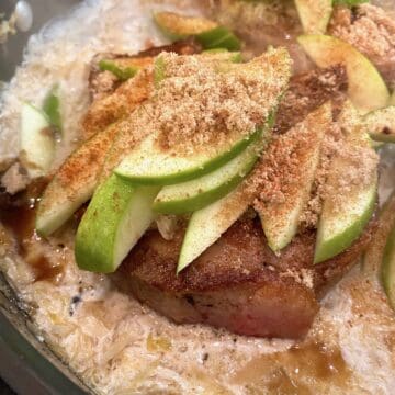 Cooked pork chops topped with sliced apples and spices in a skillet.