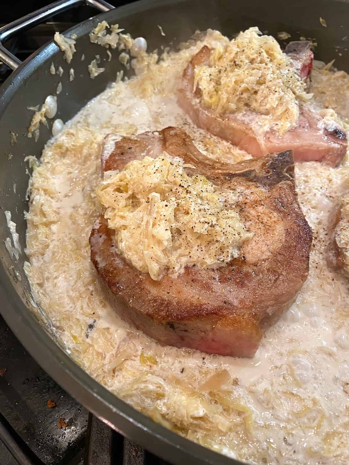 Cooked pork chops with a dollop of sauerkraut on top of each one, in a skillet.