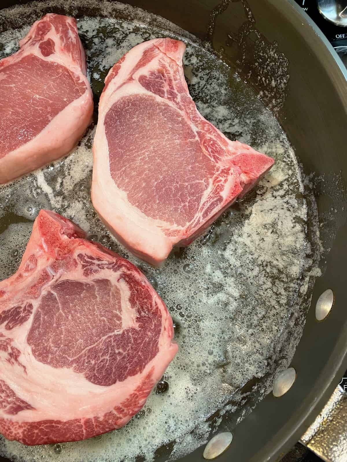 Pork chops in a skillet on the stove. 