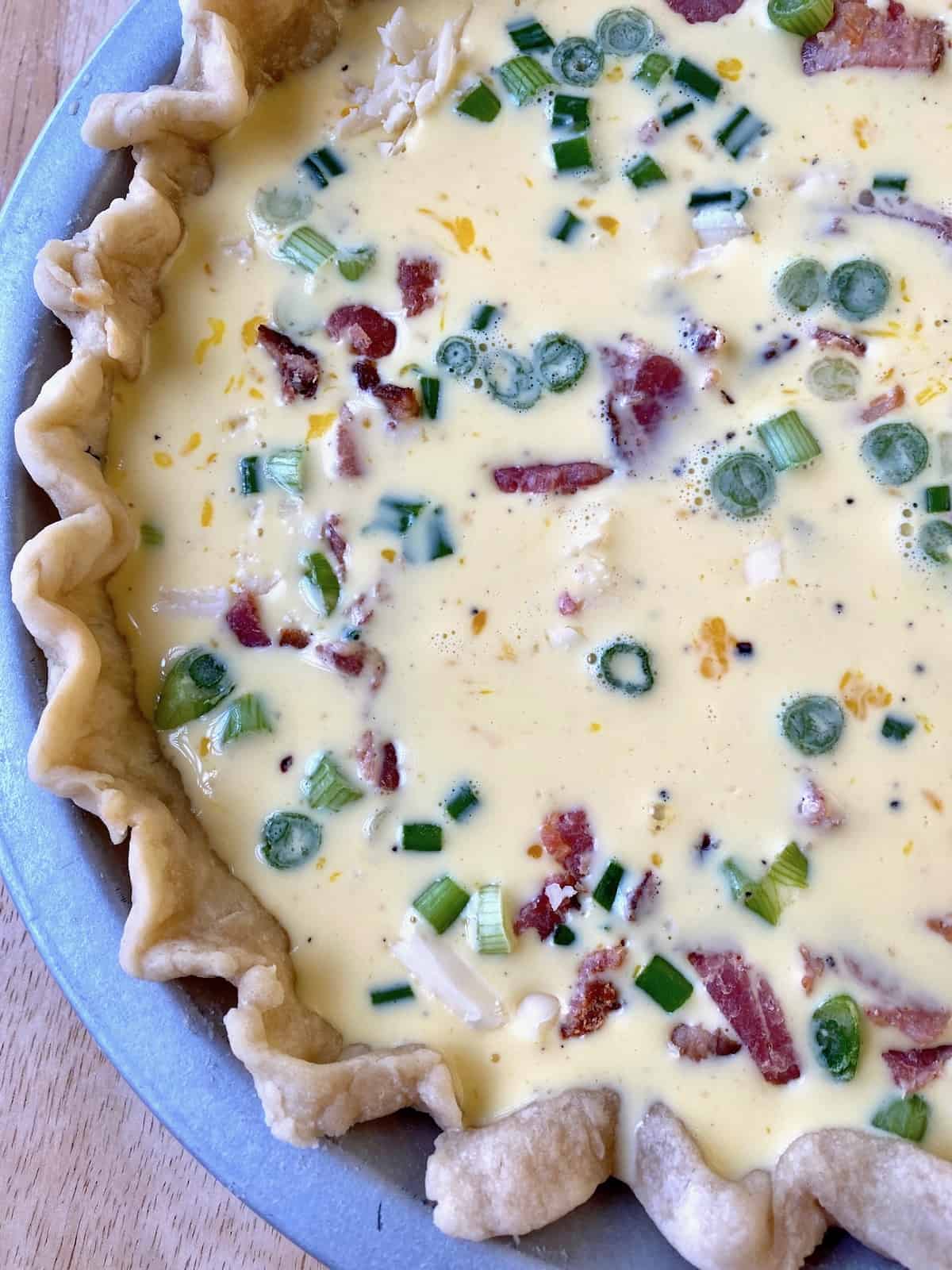 Unbaked quiche with bacon and diced green onions.