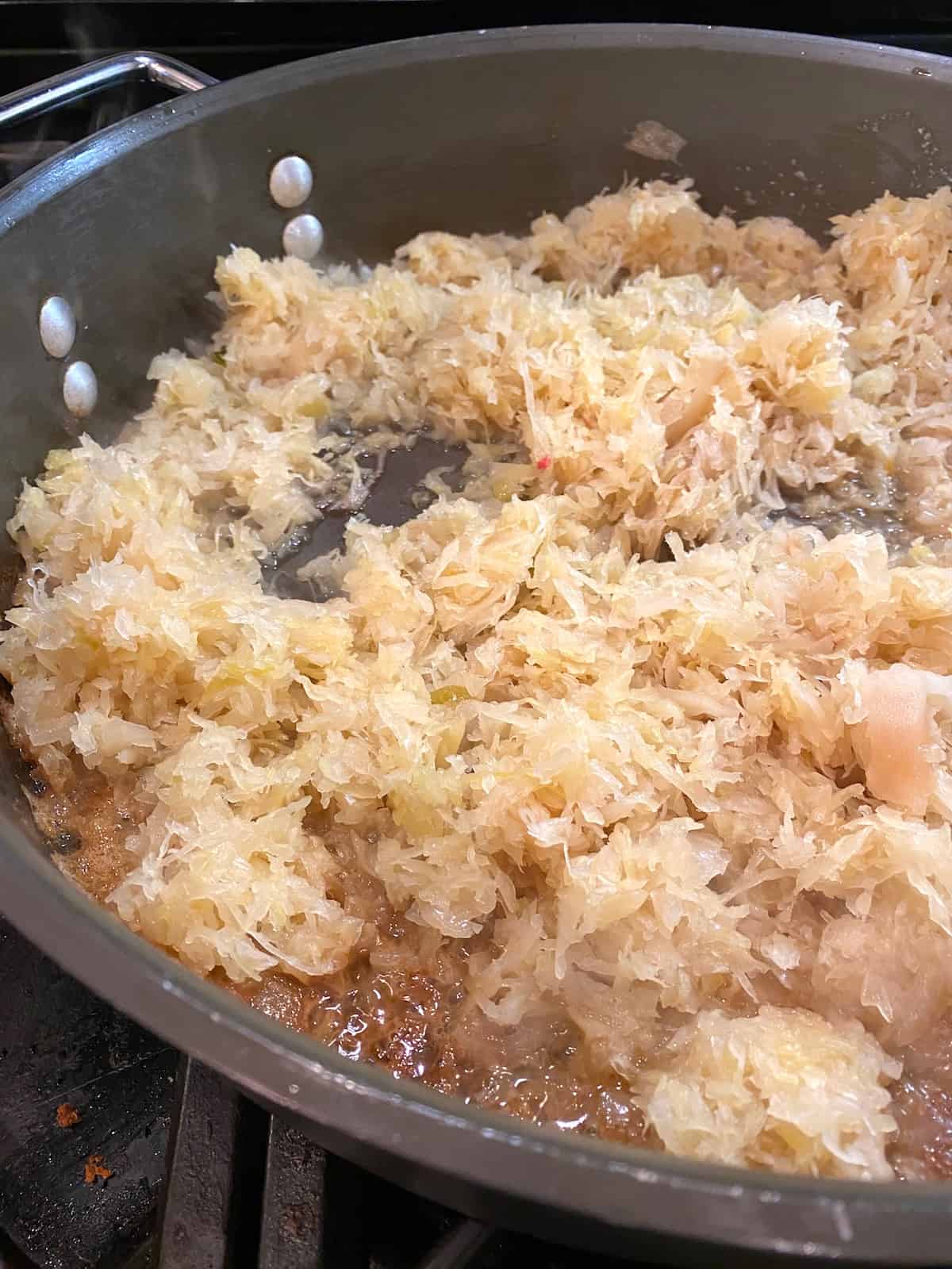 Sauerkraut cooking in melted butter in a skillet on the stove. 