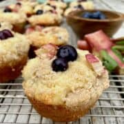 Baked muffin on a cooling rack with two blueberries and sugar on top.