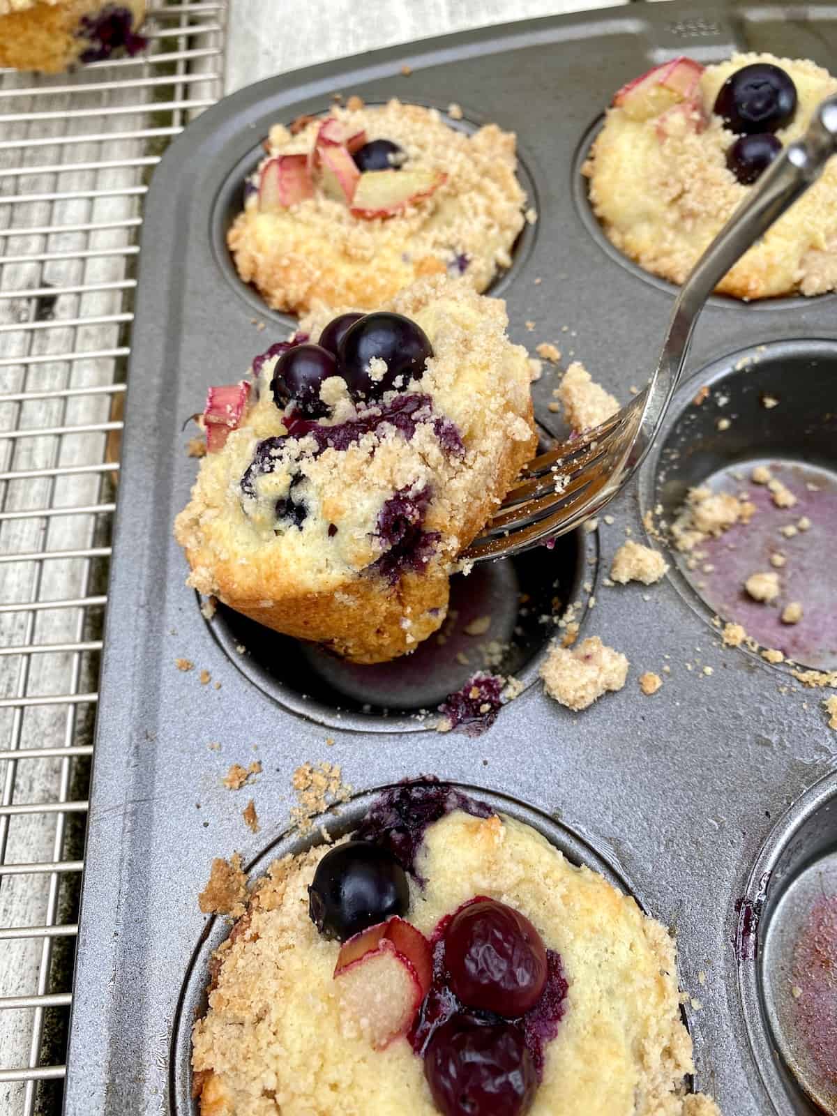 A fork removing a muffin from a muffin pan.