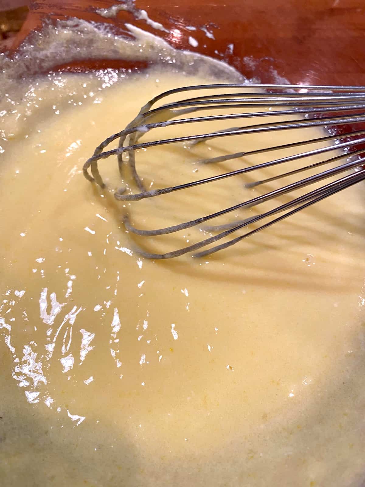 A whisk in a bowl, blending egg, sugar, butter and yogurt.