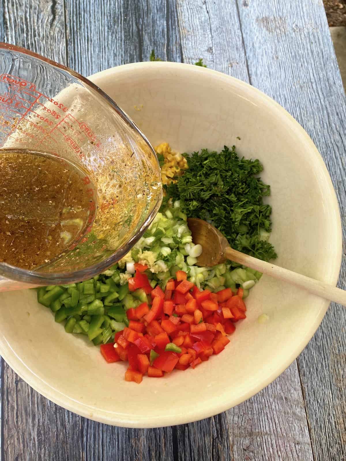 Salad dressing in a measuring cup about to be poured over the vegetables for the pasta salad. 