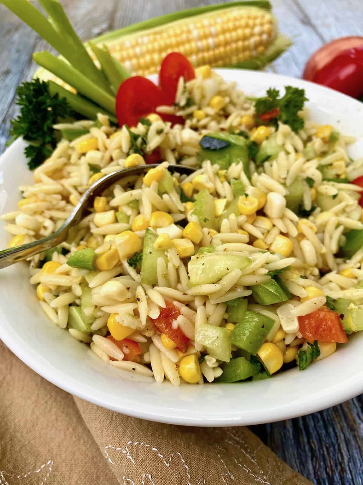 Sweet corn pasta salad in a bowl with a fresh ear of corn in the background.