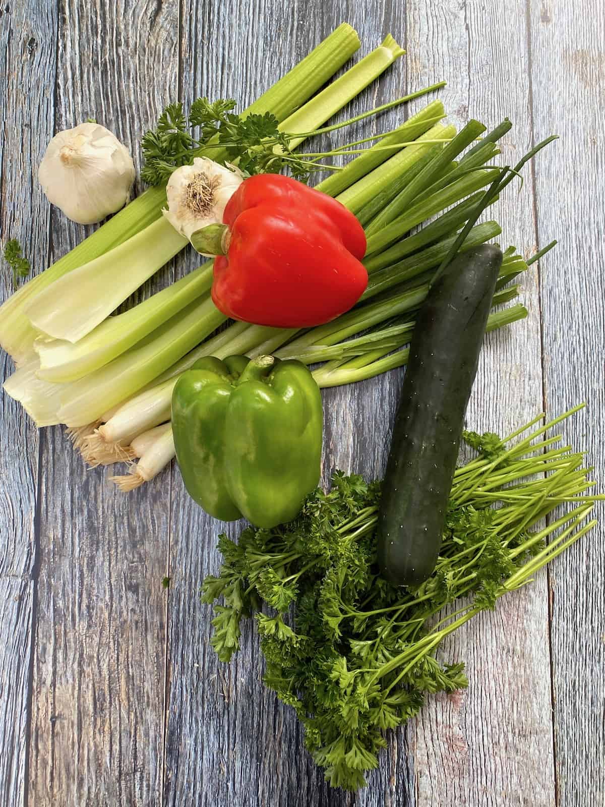 Veggies including celery, green onion, cucumber and parsley on a piece of wood. 