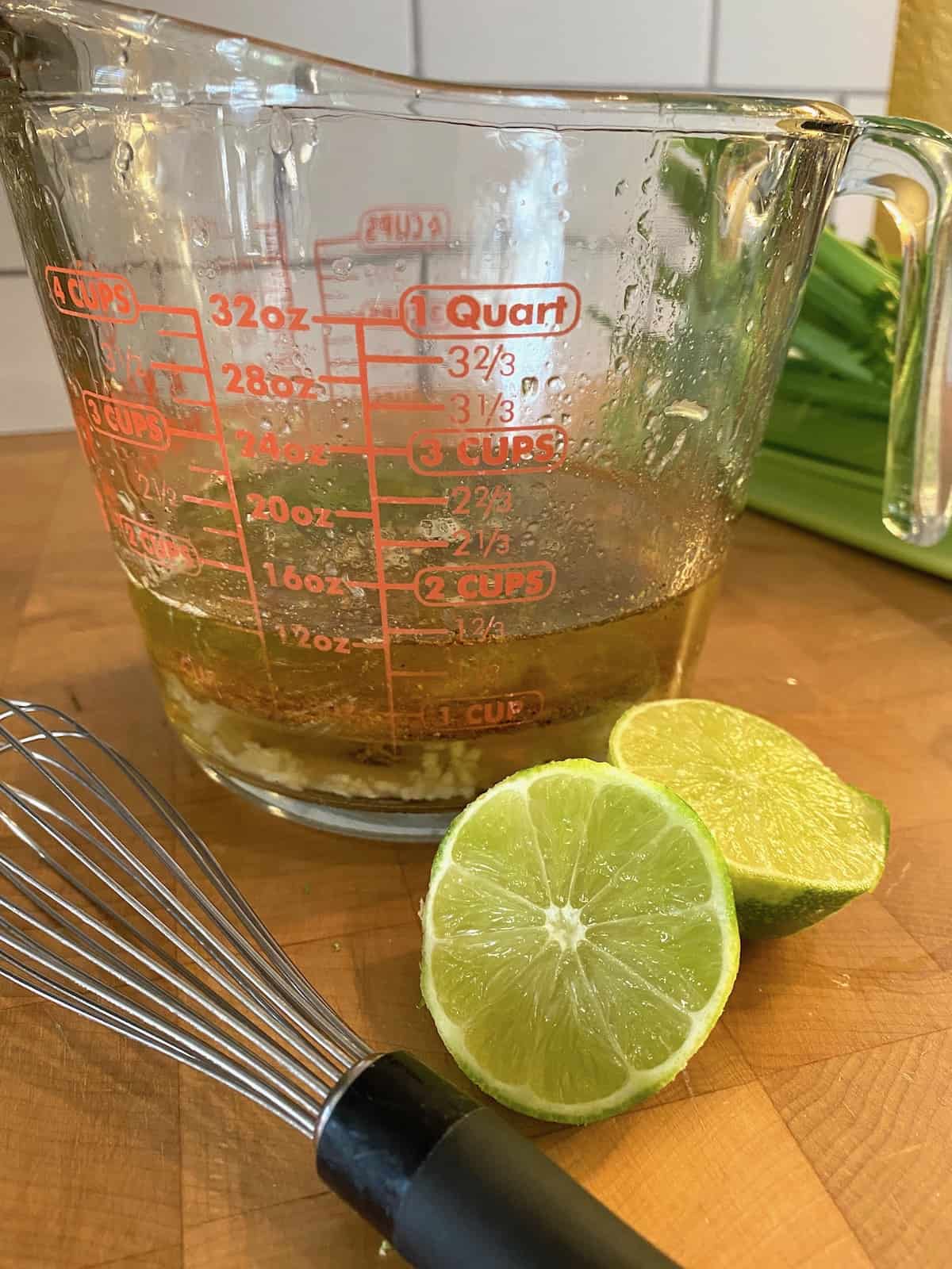 A 4-cup glass measuring cup with a lime cut in half and a whisk on the side. 