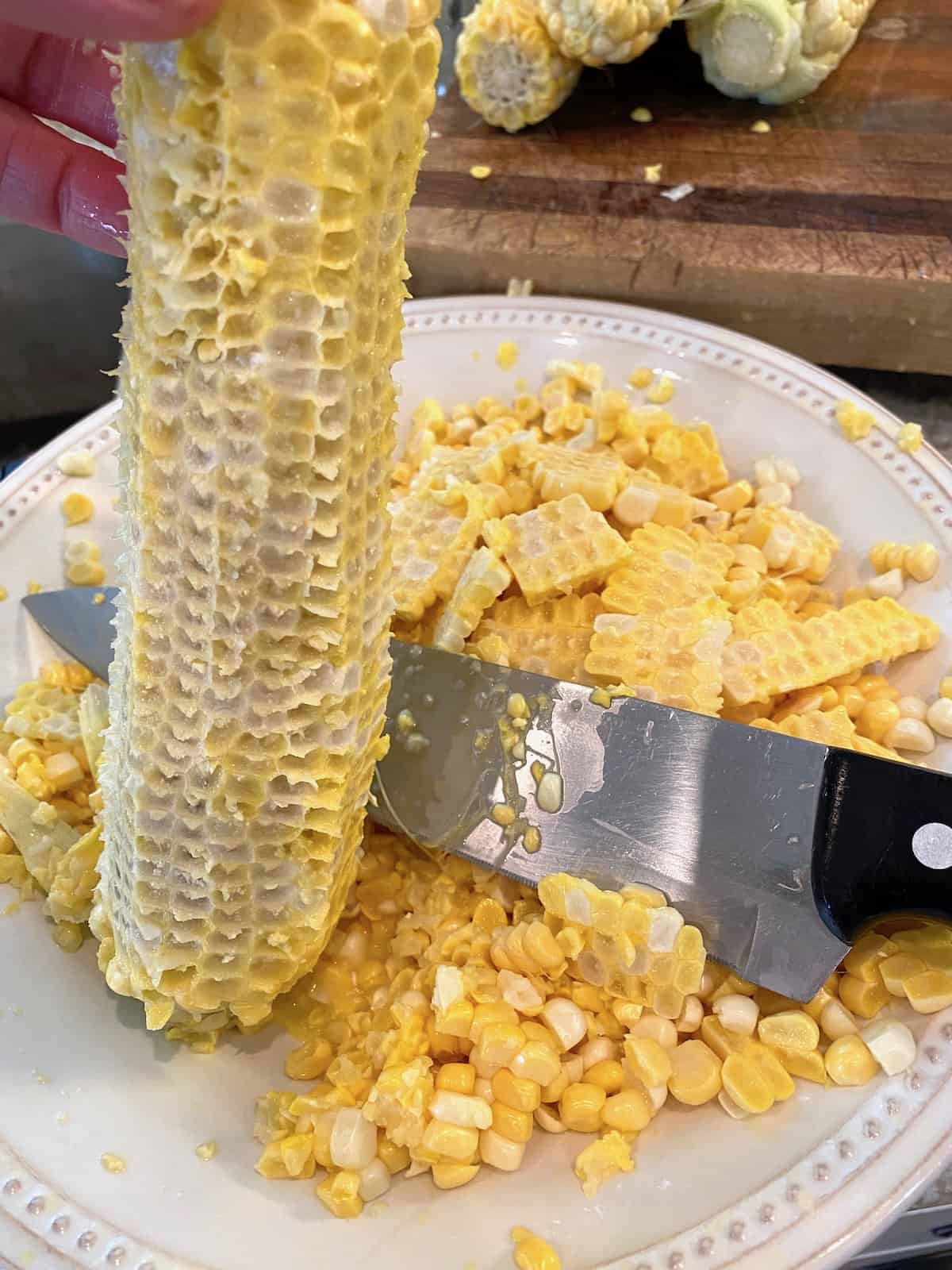 A cob of corn and a sharp knife on a plate with fresh corn.