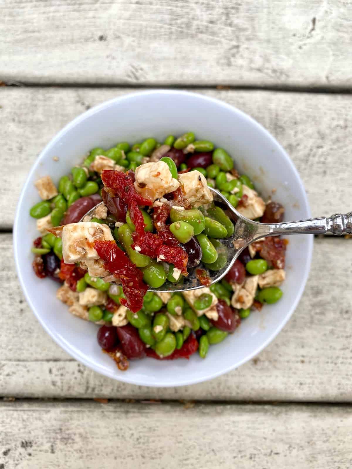 A small bowl full of edamame salad with a spoon serving up on small portion.