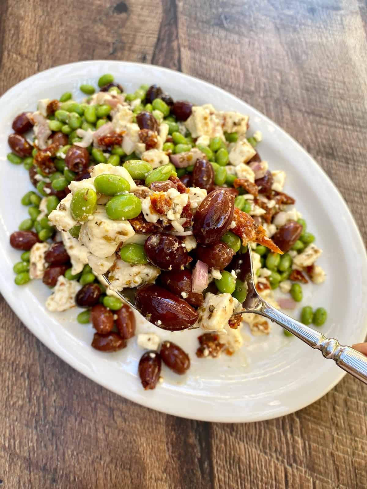 Edamame salad on a plate with a large spoon scooping out a portion of salad.