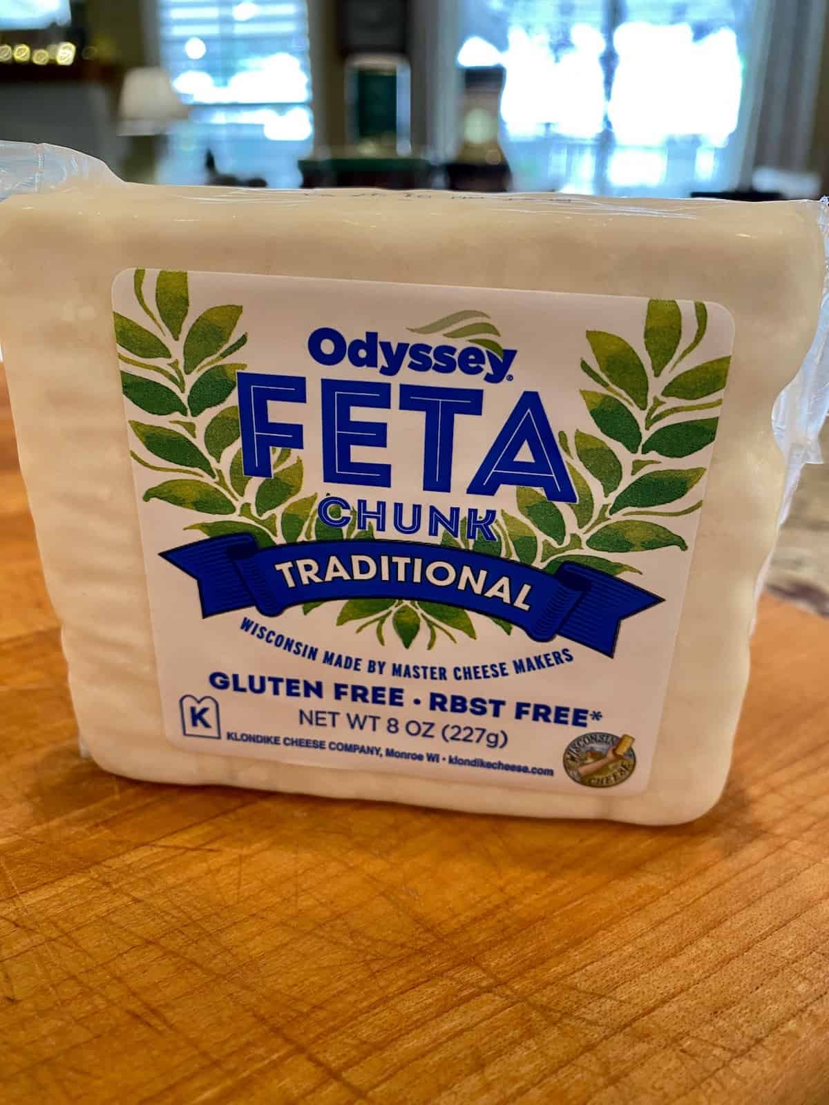 One packaged, block of feta cheese on a cutting board.