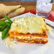 A serving of sweet potato lasagna on a plate with a glass of water off to the side.