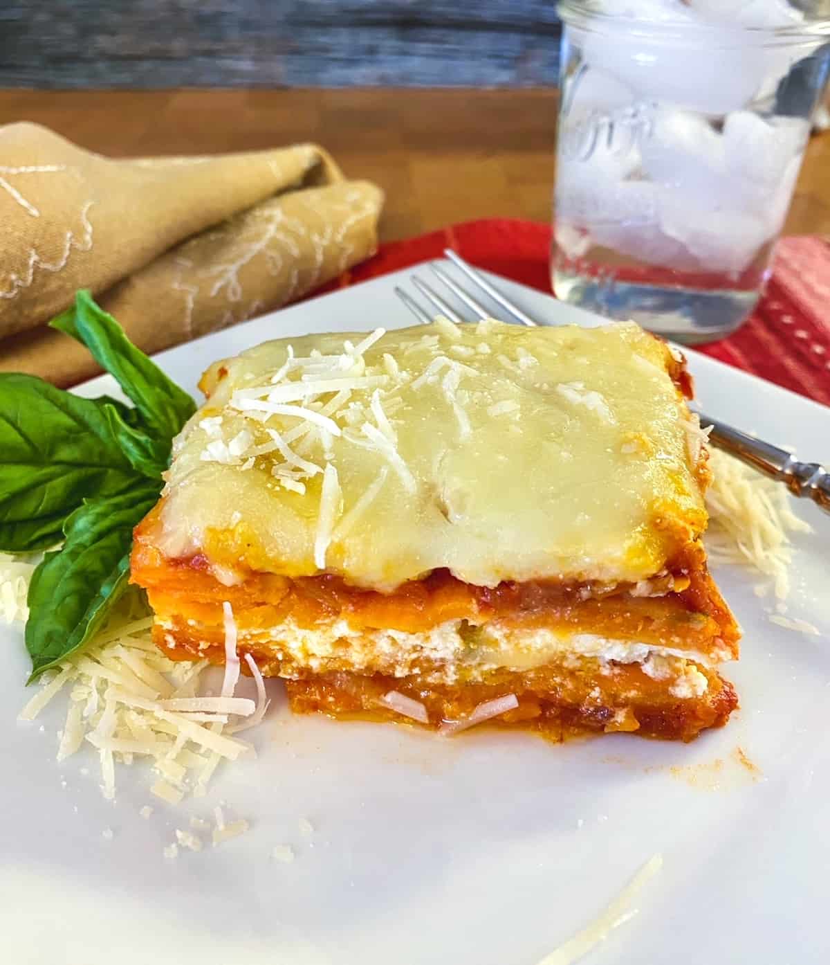 A serving of sweet potato lasagna on a plate with a glass of water off to the side.
