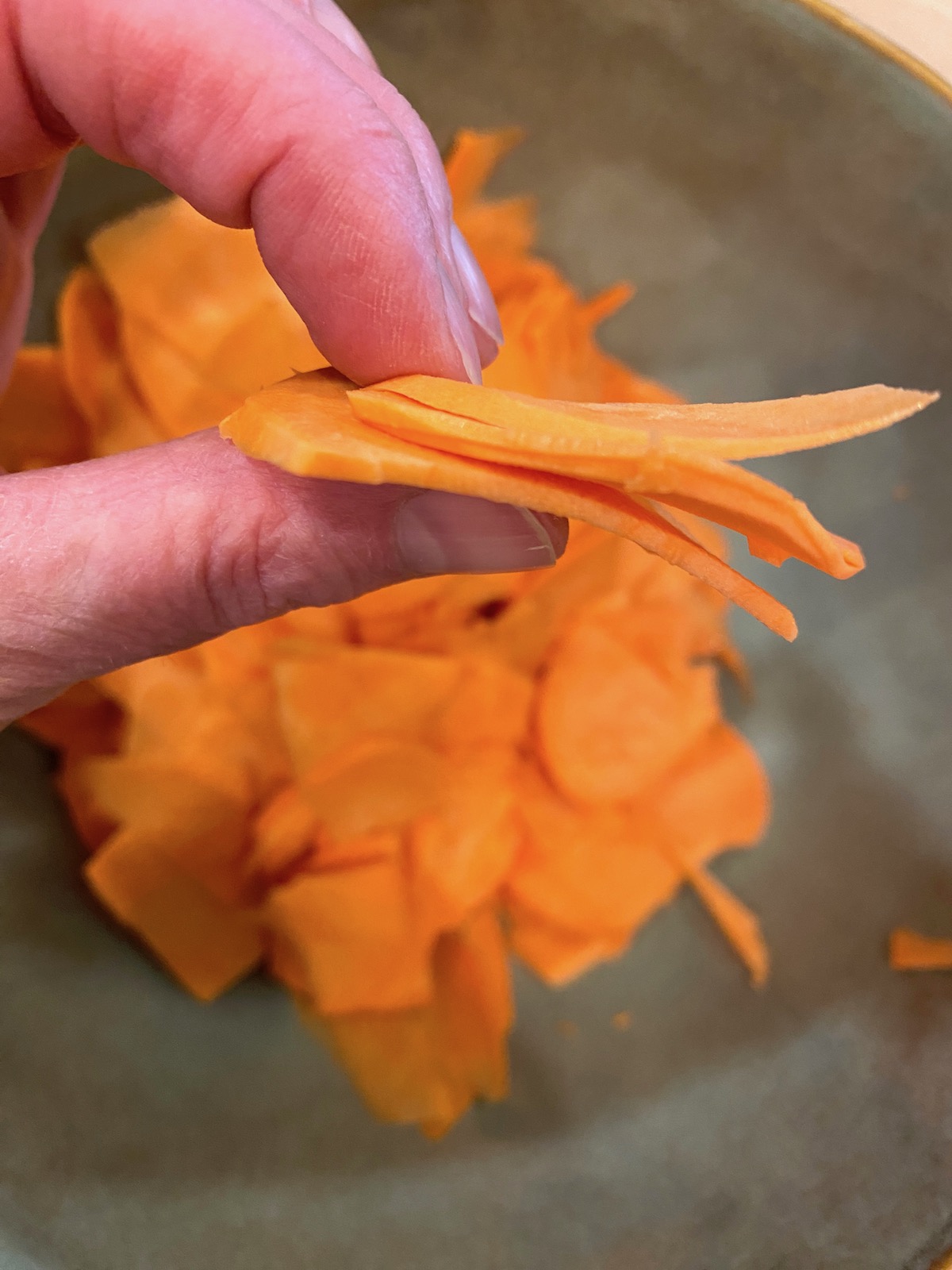 A hand holding sliced sweet potatoes, sliced very thin.