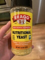 A hand holding a jar of nutritional yeast.