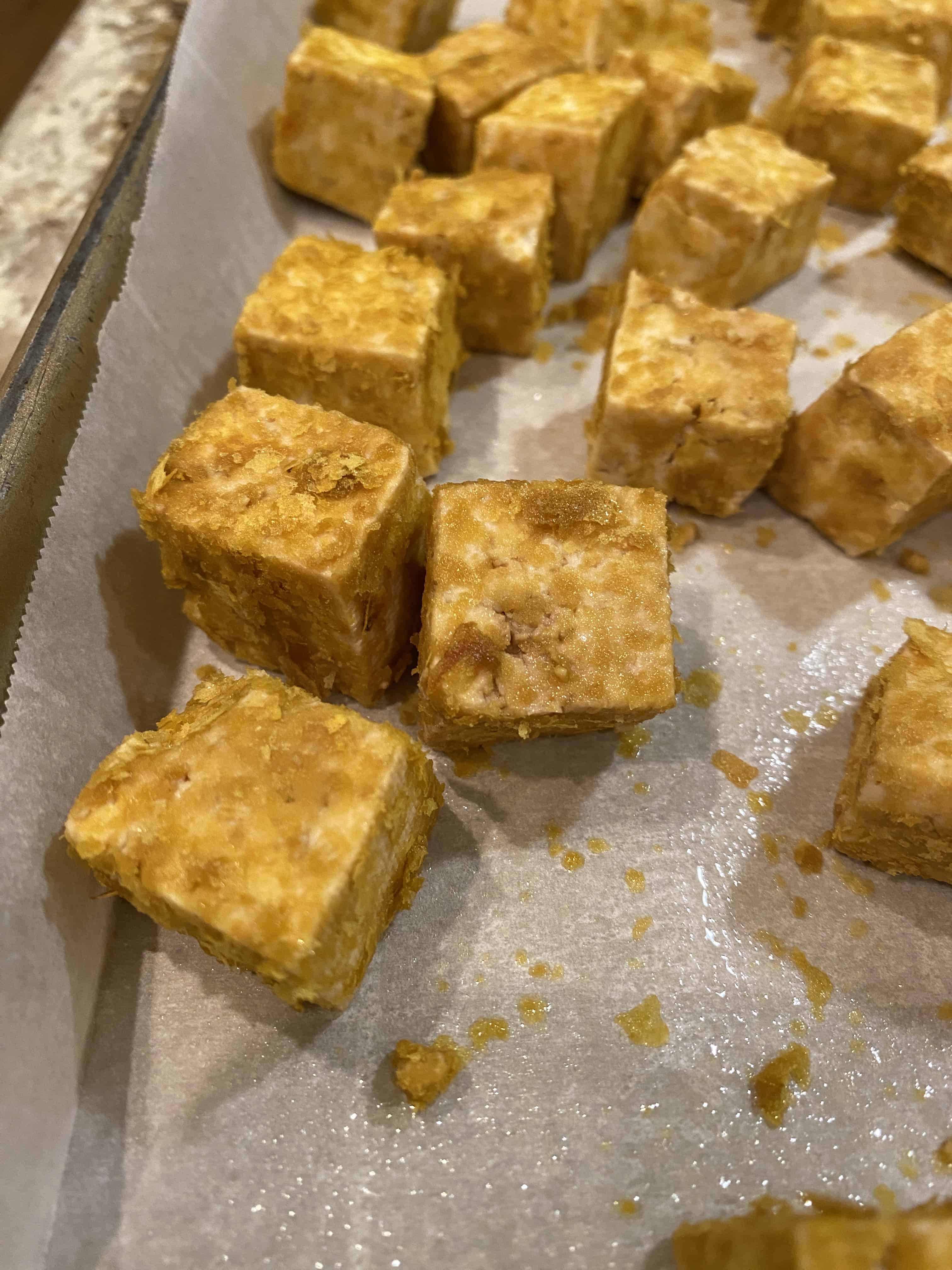 Diced tofu chunks with breading spread out on a piece of parchment paper on a baking sheet.